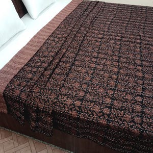 May include: A black and brown kantha quilt with a floral pattern. The quilt is folded and displayed on a bed.
