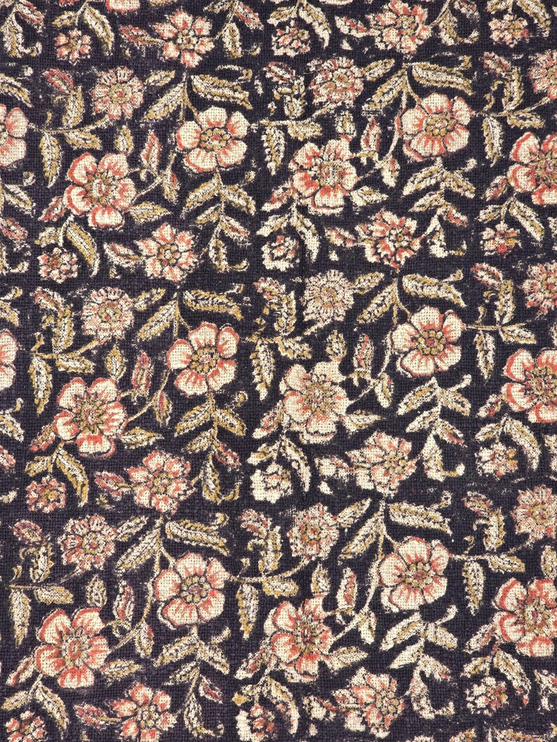 May include: Close-up of a fabric with a repeating floral pattern. The design features peach-coloured flowers with dark centres and light beige leaves on a dark navy blue background. The pattern is dense and detailed.