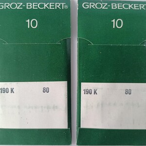 Puede incluir: Dos cajas de embalaje verdes y blancas para agujas de máquina de coser. Las cajas están etiquetadas con "GROZ-BECKERT" y "10". Las cajas también tienen los números "190 K" y "80" impresos en ellas.