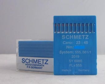 Puede incluir: Una caja de plástico azul que contiene un paquete de agujas para máquina de coser. La caja tiene el texto "SCHMETZ" y "HERZOGENRATH FR GERMANY" impreso en ella. Las agujas están etiquetadas con el texto "SCHMETZ", "Canu: 23:45", "Nm:", "System: 555, 561/1", "2019", "SY 6985", "FLx555", "Made in Germany".
