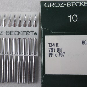 Puede incluir: Un paquete de agujas para máquina de coser Groz-Beckert. Las agujas plateadas están en un soporte de plástico blanco. El paquete incluye el texto "GROZ-BECKERT" y "10". La caja también muestra "80/12", "134 K", "797 KH" y "PF x 797".