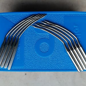 May include: A blue plastic case with a set of 10 curved needles. The needles are silver and have a slight bend at the tip. The case has the word "101" printed on it.