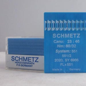 May include: A blue plastic package of sewing machine needles labeled "SCHMETZ" with the text "Canu: 23:46 Nm: 80/32 System: 551 561/2 2020, SY 6986 FLx551 Made in Germany" and a smaller blue plastic package labeled "SCHMETZ HERZOGENRATH FR GERMANY"