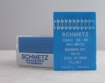 Puede incluir: Un paquete de plástico azul de agujas para máquina de coser etiquetado como "SCHMETZ" con el texto "Canu: 23:46 Nm: 80/32 System: 551 561/2 2020, SY 6986 FLx551 Hecho en Alemania" y un paquete de plástico azul más pequeño etiquetado como "SCHMETZ HERZOGENRATH FR ALEMANIA"