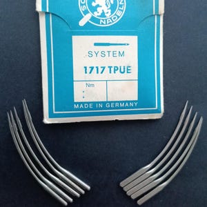 May include: A package of 1717 TPU sewing needles, made in Germany. The package is blue and white with the text "SYSTEM 1717 TPU" and a lion logo. The needles are silver and curved.