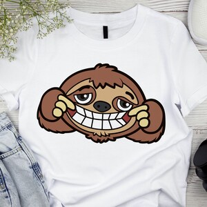 May include: White t-shirt with a cartoon image of a brown sloth with a mischievous grin and a toothy smile. The sloth is covering one eye with its hand.