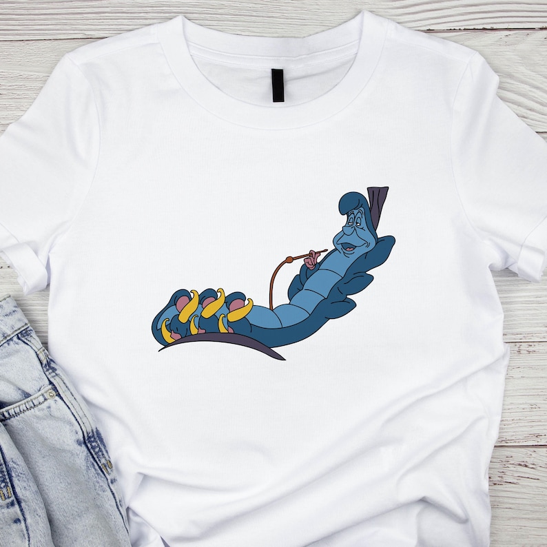 Puede incluir: Camiseta blanca con una oruga de dibujos animados azul y amarilla fumando una pipa. La oruga lleva una corona y tiene una expresi&oacute;n de sorpresa.