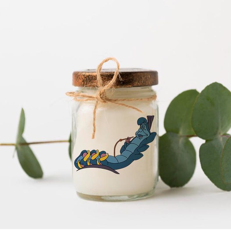 Puede incluir: Un tarro de vidrio para velas con tapa de madera y un lazo de cuerda marr&oacute;n. La vela es blanca y presenta una imagen de dibujos animados de la oruga de Alicia en el Pa&iacute;s de las Maravillas fumando una pipa de agua.
