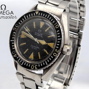 May include: A vintage Omega Seamaster De Ville wristwatch with a black dial and silver-tone metal band. The watch face has gold-colored hour markers and hands. The bezel is black with white markings. The watch is an automatic.