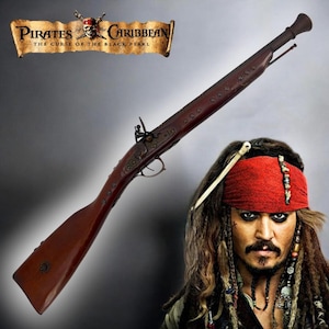 Puede incluir: Réplica de un fusil mosquete marrón oscuro de la película "Piratas del Caribe: La Maldición de la Perla Negra". El fusil tiene una culata y cañón de madera, con detalles metálicos. El título de la película se muestra arriba.
