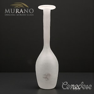 May include: A frosted glass vase with a long neck and a rounded base. The vase has a small, circular opening at the top. The Murano glass vase is labeled with the text "MURANO ORIGINAL MURANO GLASS". The word "Cenedese" is also visible.