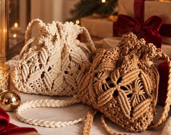 May include: Two macrame drawstring pouches, one in cream and one in tan, featuring intricate knotted geometric patterns and braided shoulder straps. Each bag has a cinched top closure with wooden bead accents, showcasing a detailed fiber art design.