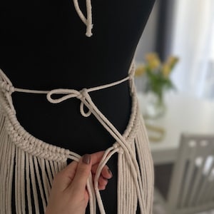 May include: A white macrame top with fringe detailing. The top is tied at the back with a bow.