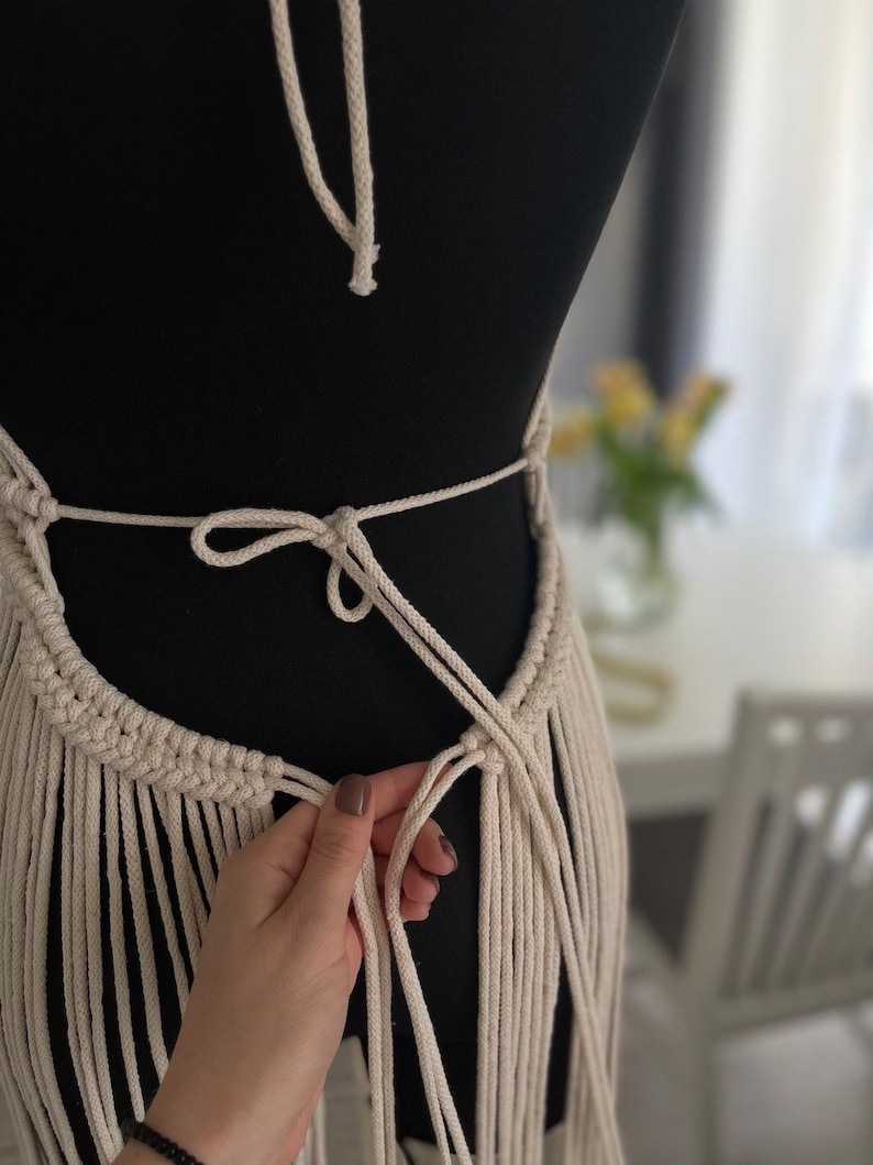 May include: A white macrame top with fringe detailing. The top is tied at the back with a bow.