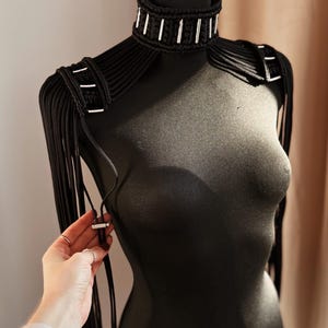 Peut inclure: Un collier ras de cou noir avec des accents argent&eacute;s et des bretelles assorties avec des franges. Le collier et les bretelles sont faits d'un cordon &eacute;pais et tiss&eacute;.