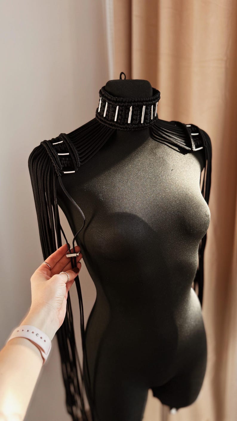 Peut inclure: Un collier ras de cou noir avec des accents argent&eacute;s et des bretelles assorties avec des franges. Le collier et les bretelles sont faits d'un cordon &eacute;pais et tiss&eacute;.