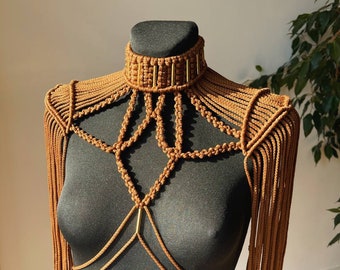 May include: A brown macrame body harness with gold accents. The harness features a choker necklace, shoulder straps, and a chest piece.
