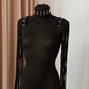 Peut inclure: Un collier ras de cou noir avec des accents argent&eacute;s et des bretelles assorties en cordon noir.