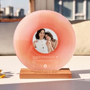 Puede incluir: Un disco de acrílico rosa con una foto de dos mujeres dentro de un marco circular. El disco está sobre una base de madera con el texto "Mamá, gracias por estar a mi lado hoy y siempre".