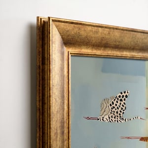 K&ouml;nnte beinhalten: Ein gerahmtes Wandbild mit einem stilisierten Vogel mit schwarz-wei&szlig;em Punktmuster im Flug vor hellblauem Hintergrund. Das Kunstwerk ist in einem breiten, strukturierten, antikgoldfarbenen Rahmen mit tiefem, abgeschr&auml;gtem Profil gefasst.