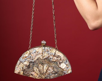May include: A fan-shaped clutch bag featuring a mosaic of iridescent shell fragments and clear crystals. The bag has a gold-toned metal frame, a top clasp with a clear crystal accent, and a thin, twisted gold-toned metal chain shoulder strap.