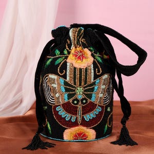May include: Black beaded drawstring bag with a butterfly and floral design. The butterfly has turquoise, brown, and white beaded wings. The bag features a black drawstring closure and tassels.