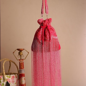 Könnte beinhalten: Eine leuchtend rosa Perlen-Kordelzugtasche mit passendem Perlenhenkel, die an einem silbernen Haken hängt. Die Tasche hat aufwendige Perlenarbeiten und eine lange Fransen aus rosa Perlen, was ein luxuriöses und auffälliges Accessoire ergibt.
