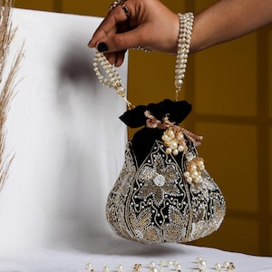 May include: A black and gold beaded handbag with a pearl handle. The bag features intricate floral patterns and is adorned with pearls and gold accents. The bag is held by a pearl-beaded handle.