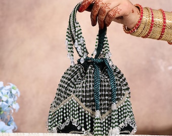 May include: A beaded drawstring bag in dark green and silver. The bag features a decorative pattern of beads and dangling crystal accents. The handle is a twisted green cord. The bag is held by a hand with henna tattoos and gold bangles.