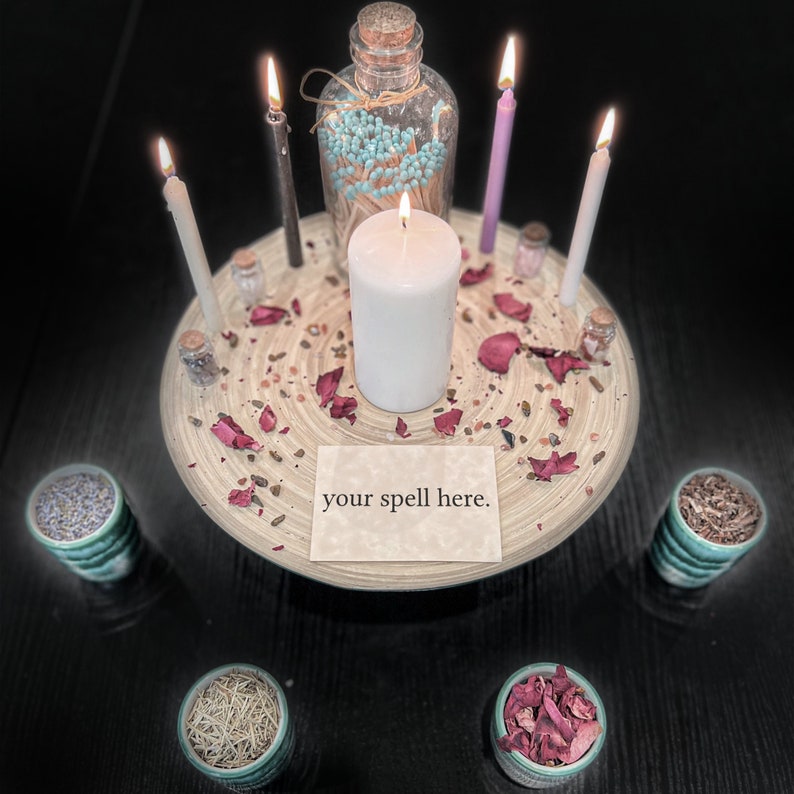 May include: A circular wooden tray holds a central white pillar candle, four smaller taper candles in white, black, and purple, a glass bottle of teal-tipped matches, small jars, and dried rose petals. A card reads your spell here.