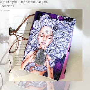 Puede incluir: Diario de viñetas inspirado en amatista con una ilustración celestial de una mujer con cabello blanco ondeante y un fondo de galaxia púrpura. El diario tiene un cierre de correa de cuero y un cristal de amatista natural.