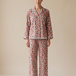 Könnte beinhalten: Ein zweiteiliger Pyjama-Set mit einem roten Erdbeermuster auf hellem Hintergrund. Das langärmlige Oberteil und die Hose haben weiße Paspeln. Der Text "NAAZBOUTIQUE01" ist auf dem Oberteil sichtbar.
