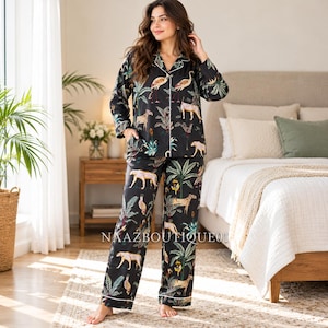 Könnte beinhalten: Ein schwarzer Pyjama bestehend aus einem langärmeligen Hemd mit Knopfleiste und einer passenden Hose, verziert mit einem Muster aus Geparden, tropischen Palmen und Blättern. Das Set ist mit einer weißen Paspelierung an Kragen und Ärmeln versehen.