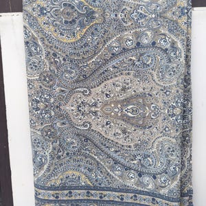 Könnte beinhalten: Ein gefalteter Stoff mit einem detaillierten Paisley-Muster in Blau-, Grau- und Gelbtönen. Der Stoff hat einen Rand mit einem sich wiederholenden Design. Die Gesamtästhetik ist vintage und dekorativ, geeignet für Heimdekoration oder Mode.
