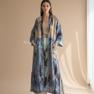 Könnte beinhalten: Ein langer, offen geschnittener Morgenmantel mit blauem und beigem Batikmuster. Der Morgenmantel hat lange Ärmel und Taschen. Der Text "NAAZBOUTIQUE01" ist auf den Morgenmantel gedruckt. Das Model trägt ein beiges Oberteil und eine weiße Hose.
