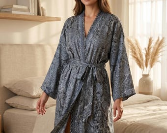 May include: A long, flowing robe with a paisley pattern in shades of blue and gray. The robe has wide sleeves and a matching tie belt. The fabric appears soft and lightweight, suitable for lounging. The robe is open in the front, revealing the legs.