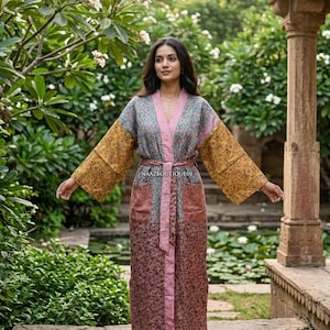 May include: A long, patterned robe with a belt. The robe features a mix of colors, including pink, gold, and blue. The sleeves are wide and the robe is open in the front. The text "NAAZBOUTIQUE01" is visible on the robe.