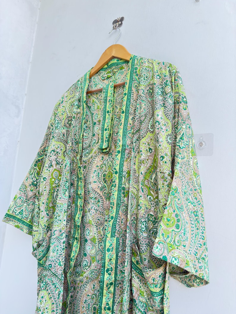 May include: A lightweight kimono-style robe featuring an intricate paisley pattern in shades of lime green, emerald, and soft peach. The garment has wide, three-quarter length sleeves, an open front design, and a matching fabric belt hanging down.