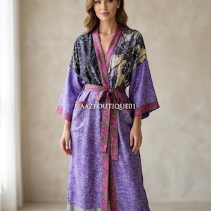May include: A long, flowing purple robe with a floral pattern and a matching belt. The robe has a contrasting panel of black, purple, and beige floral print at the shoulders and sleeves. The text "NAAZBOUTIQUE01" is visible on the robe.