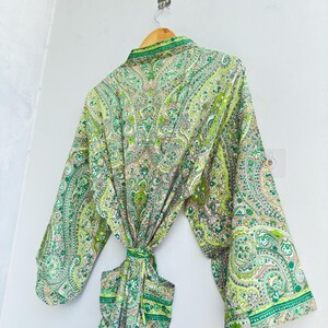 May include: A long-sleeved robe featuring a vibrant green and white paisley pattern. The garment includes a matching fabric tie belt at the waist, wide sleeves, and a folded collar, showcasing an intricate, repeating floral and teardrop design.
