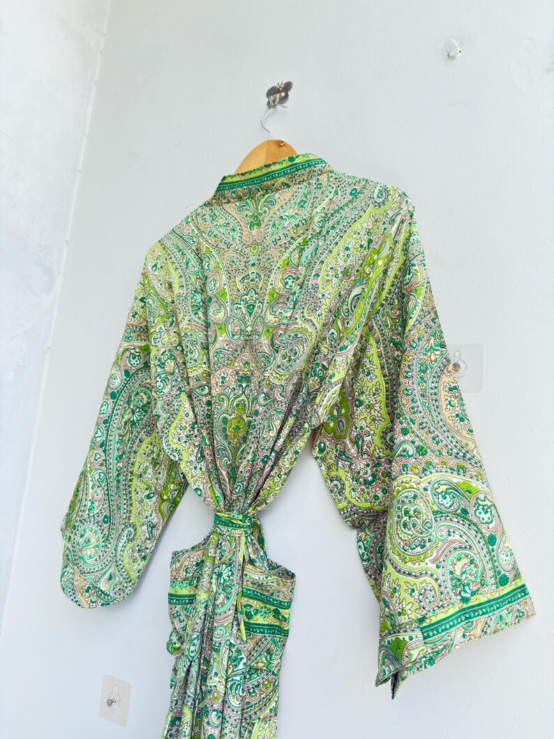 May include: A long-sleeved robe featuring a vibrant green and white paisley pattern. The garment includes a matching fabric tie belt at the waist, wide sleeves, and a folded collar, showcasing an intricate, repeating floral and teardrop design.