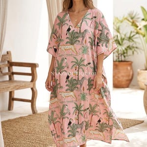 Puede incluir: Vestido caftán rosa con cuello en V con estampado de jungla de cebras, leopardos, tucanes y palmeras. El vestido tiene mangas cortas y un corte holgado. El texto "Protected by NAAZBOUTIQUE01 - Original Design" es visible.