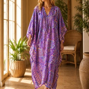 Könnte beinhalten: Ein bodenlanges, violettes Kaftan-Kleid mit einem lebendigen Patchwork-Muster aus Blumen- und geometrischen Motiven in Blau-, Rosa- und Orangetönen. Das Kleidungsstück hat einen V-Ausschnitt mit Kordelzug und weite, fließende Kimono-Ärmel.