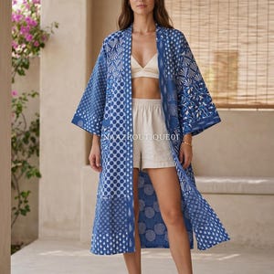 May include: A long, flowing blue and white patterned robe with a variety of geometric designs. The robe is open in the front and worn over a white top and shorts. The text "NAAZBOUTIQUE01" is visible on the robe.