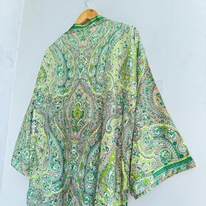 May include: A lightweight kimono-style robe featuring an intricate paisley pattern in shades of lime green, emerald, and soft pink. The garment has wide, three-quarter length sleeves, a shawl collar, and a smooth, flowing drape hanging from a hanger.