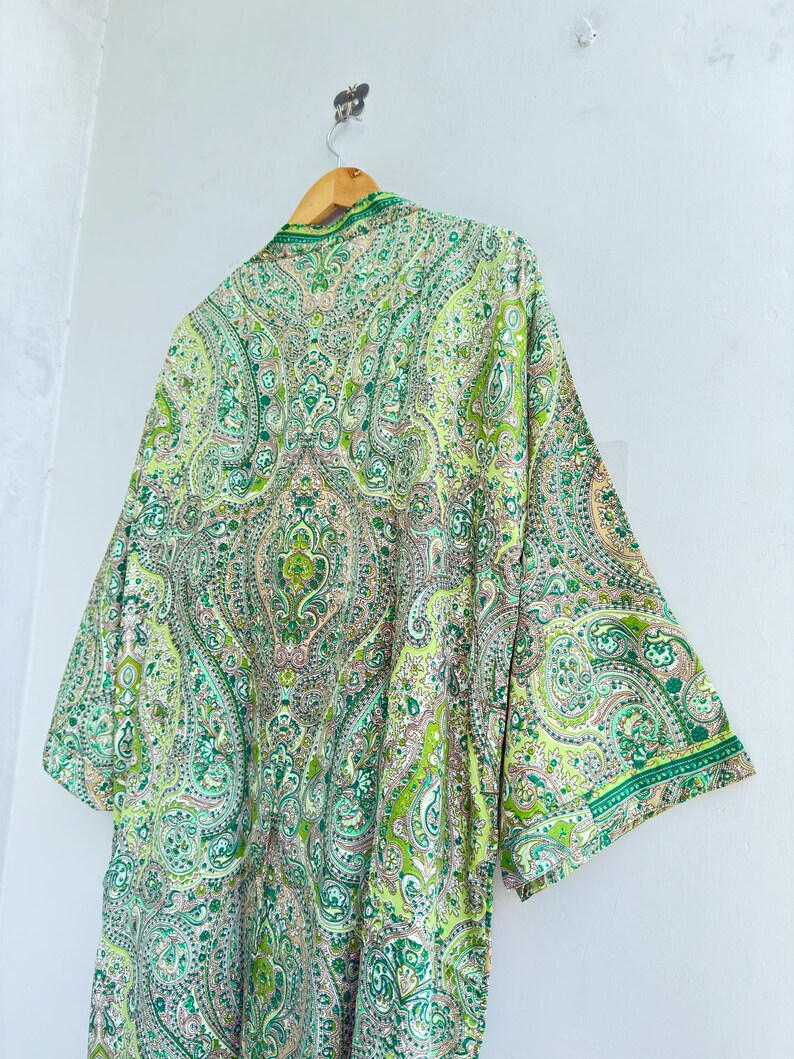 May include: A lightweight kimono-style robe featuring an intricate paisley pattern in shades of lime green, emerald, and soft pink. The garment has wide, three-quarter length sleeves, a shawl collar, and a smooth, flowing drape hanging from a hanger.