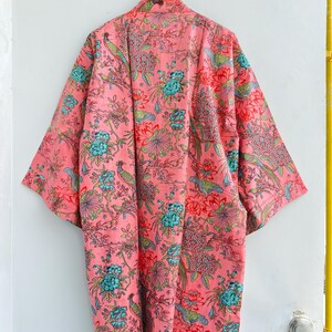 May include: A long-sleeved kimono robe in a vibrant coral pink hue, featuring an intricate all-over print of teal blue flowers, green foliage, and small birds perched on branches. The garment has a wide, open front design and loose sleeves.