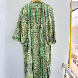 May include: A long-length kimono robe featuring a vibrant green and light yellow paisley pattern throughout. The garment has wide sleeves, an open front design with a matching fabric belt, and a contrasting dark green trim along the edges.