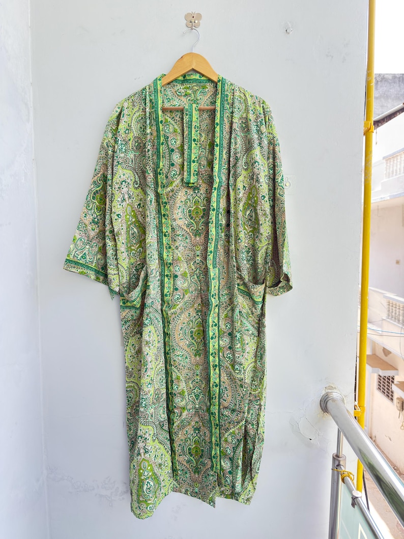 May include: A long-length kimono robe featuring a vibrant green and light yellow paisley pattern throughout. The garment has wide sleeves, an open front design with a matching fabric belt, and a contrasting dark green trim along the edges.