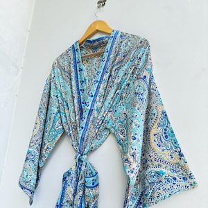 Peut inclure: Un peignoir kimono léger arborant un motif cachemire vibrant dans des tons turquoise, bleu roi et beige. Le vêtement présente des manches larges et amples, une ceinture à nouer assortie à la taille et un col structuré, suspendu sur un cintre en bois.